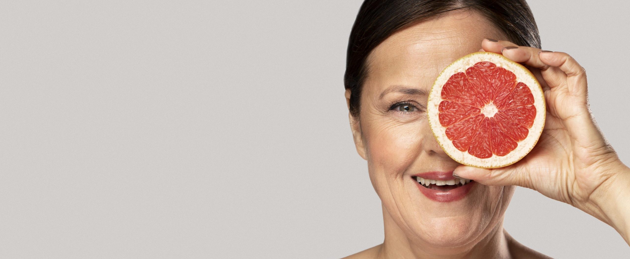 smiley-elder-woman-covering-her-eye-with-half-grapefruit